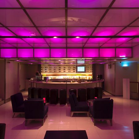 帕色哇公主酒店【SHA Extra Plus】 曼谷 外观 照片 The photo shows a modern bar interior with a sleek design. The lighting features a pink hue that illuminates the ceiling, creating a vibrant atmosphere. In the center, there is a rounded bar counter with a well-stocked shelf behind it. The seating ar