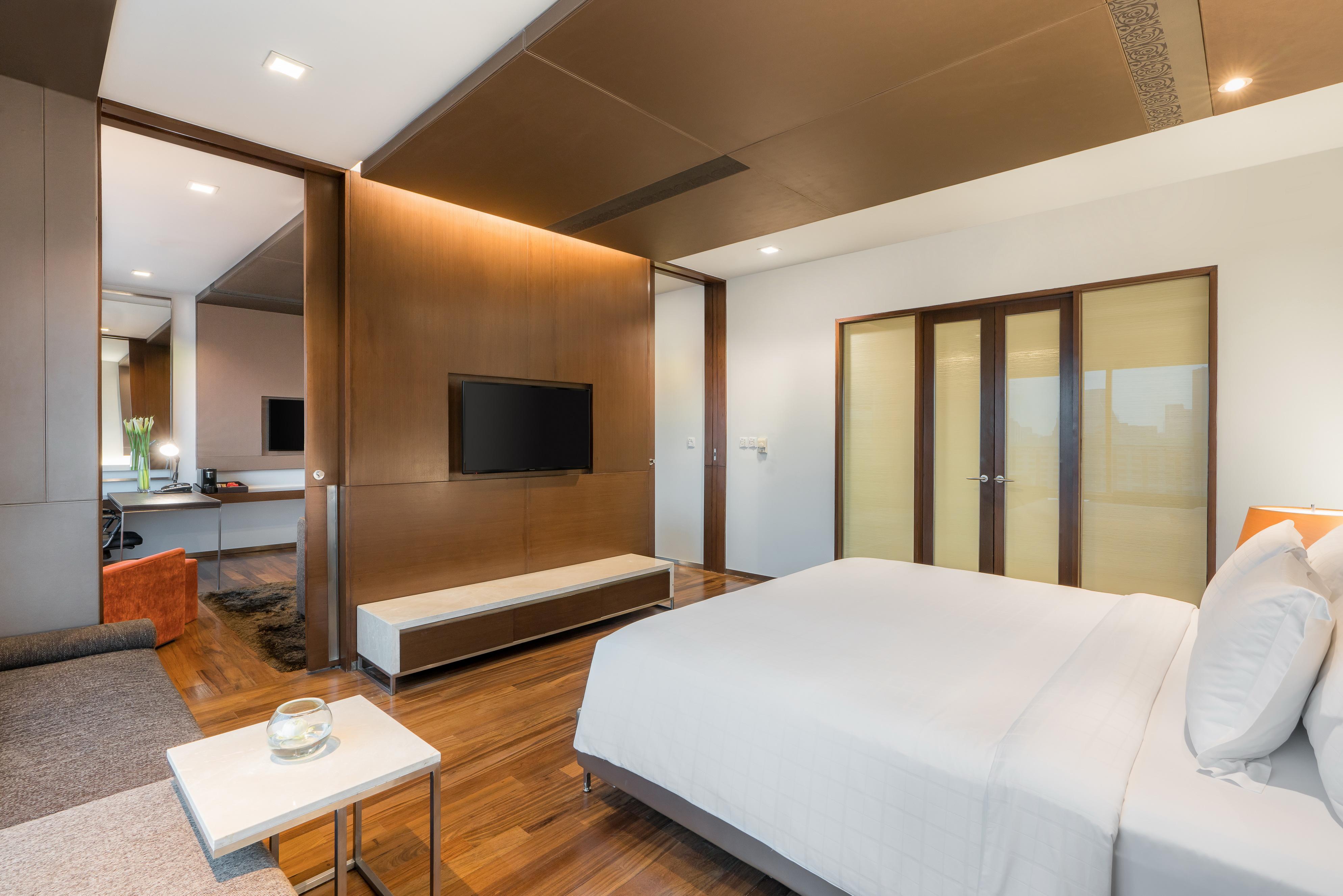 帕色哇公主酒店【SHA Extra Plus】 曼谷 外观 照片 The photo shows a modern and stylish bedroom. It features a comfortable bed with white bedding, a sleek wooden floor, and a minimalistic design. There's a large television mounted on the wall opposite the bed. In the background, there are glass doors