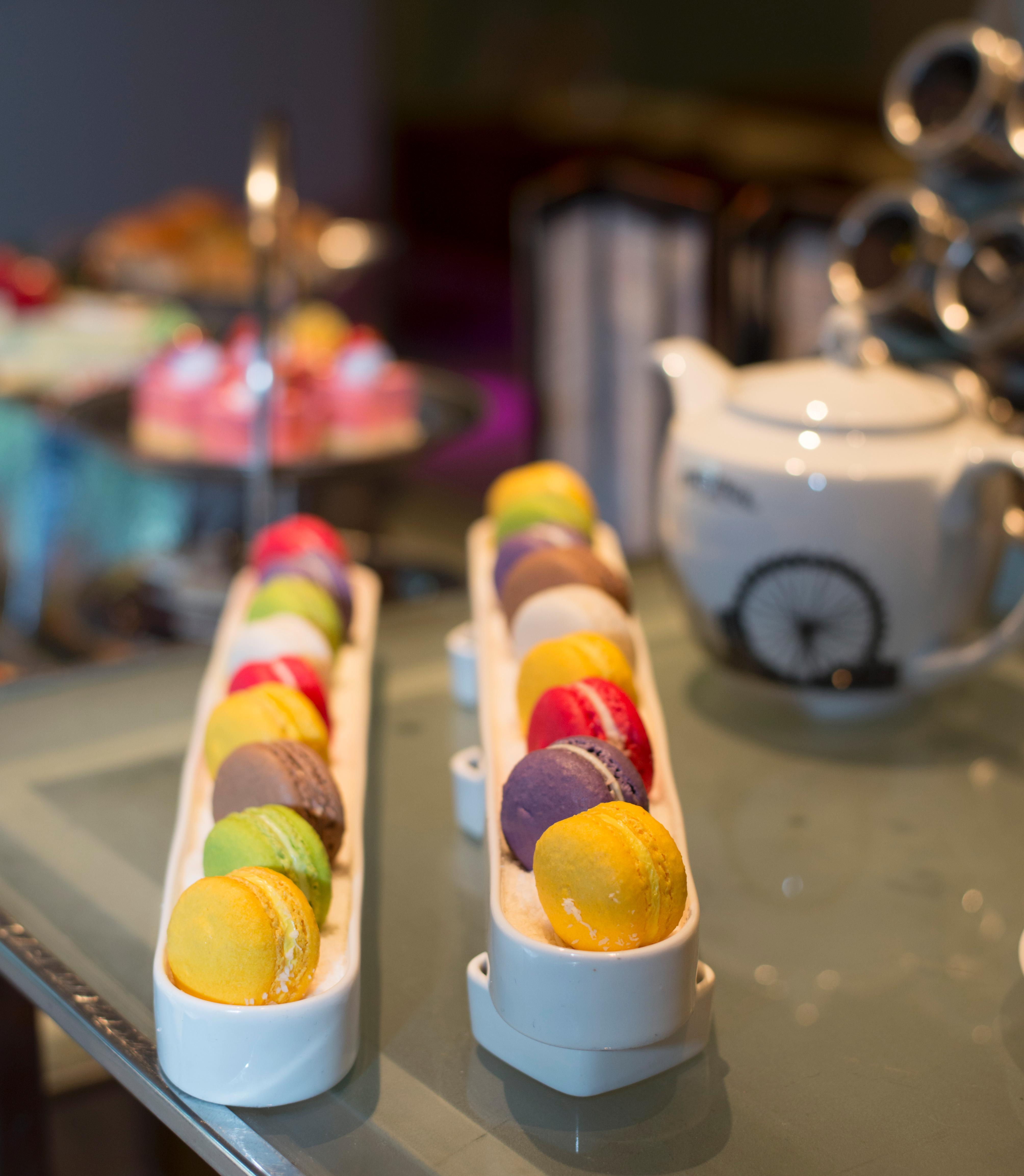 帕色哇公主酒店【SHA Extra Plus】 曼谷 外观 照片 The photo showcases an elegant display of macarons arranged in two long, narrow trays. The macarons come in a variety of colors, including yellow, green, pink, purple, and orange, suggesting a range of flavors. In the background, there is a white tea