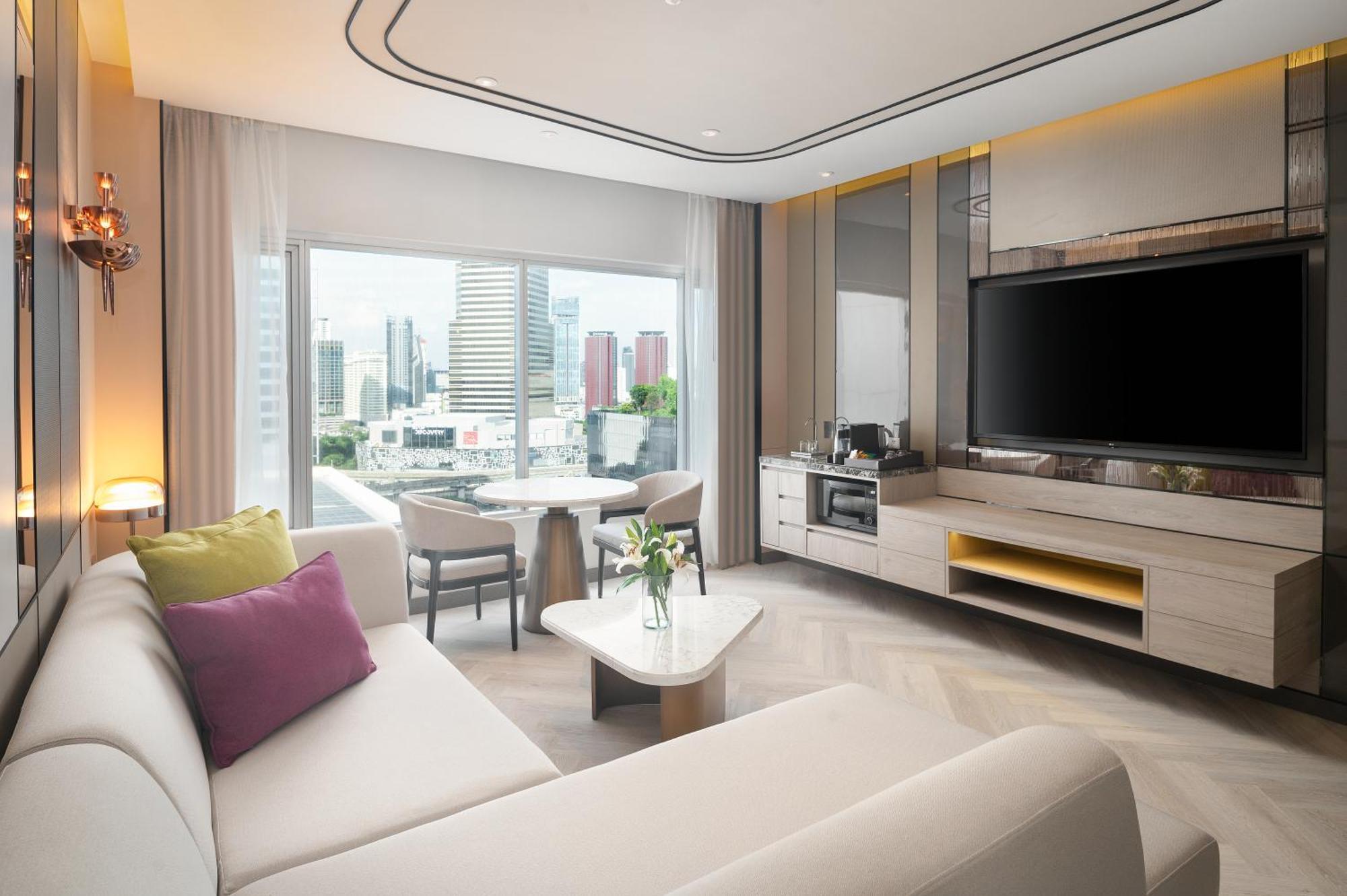 帕色哇公主酒店【SHA Extra Plus】 曼谷 外观 照片 The photo shows a modern and stylish hotel room or living area. There's a light-colored sofa with decorative pillows in shades of purple and beige. In front of the sofa, there's a small coffee table. To one side, there is a dining table with chairs, 