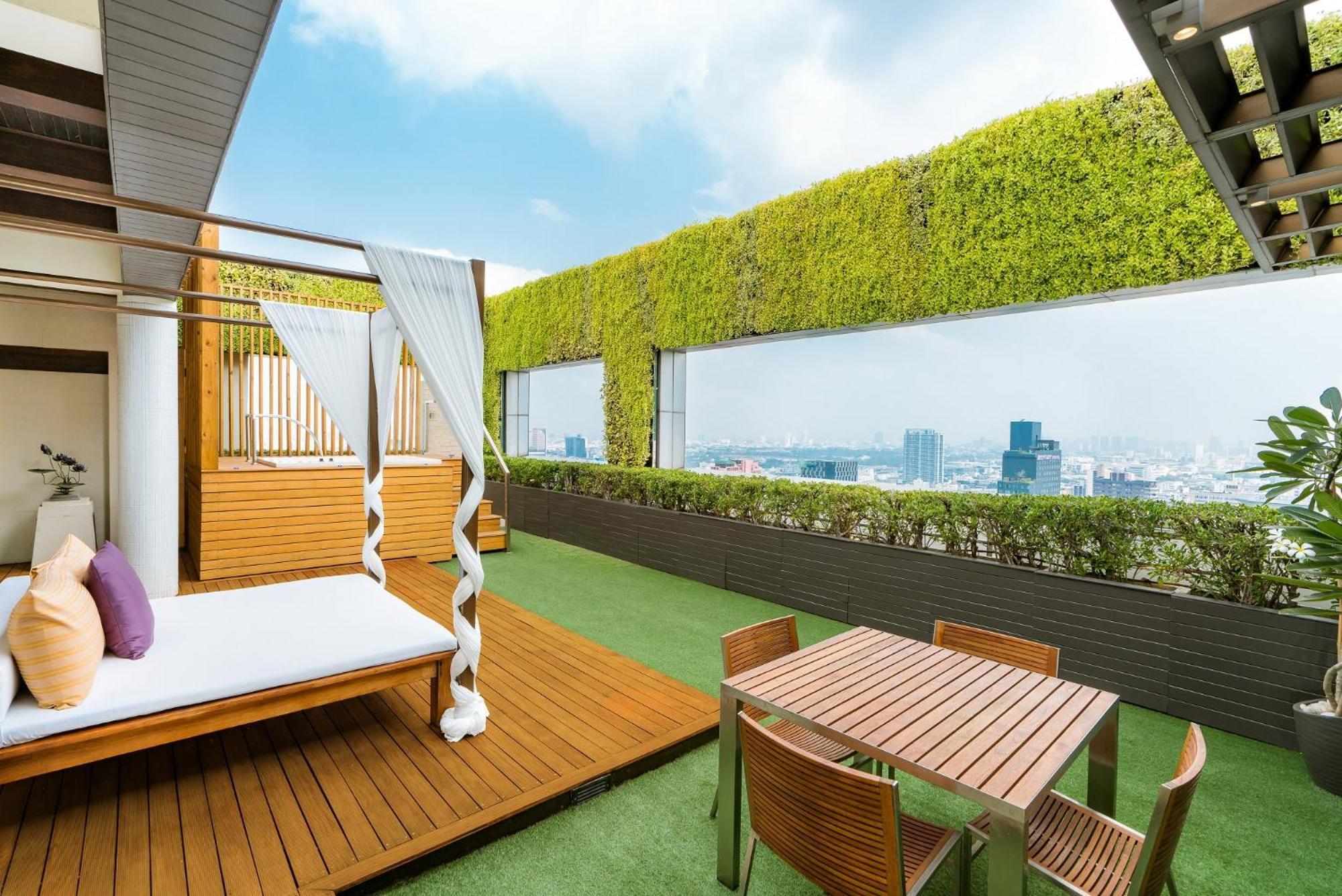 帕色哇公主酒店【SHA Extra Plus】 曼谷 客房 照片 The photo displays a modern rooftop terrace with a lush, green wall and panoramic views of a city skyline. The area features a wooden deck with a white, draped lounging bed, creating a relaxing space. In addition, there’s a small dining table with se